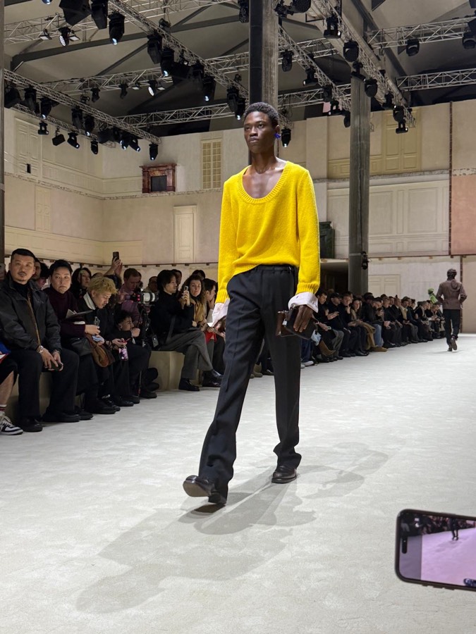 Model in a yellow knit walking a runway show, front row either side