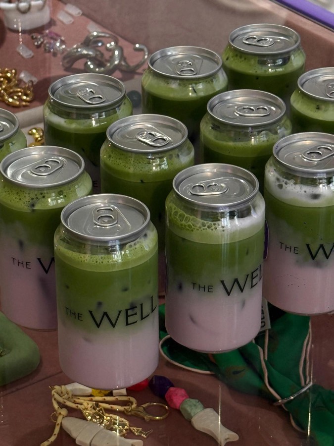 Rows of layered matcha drinks in clear cans printed with The Well, among colourful jewellery